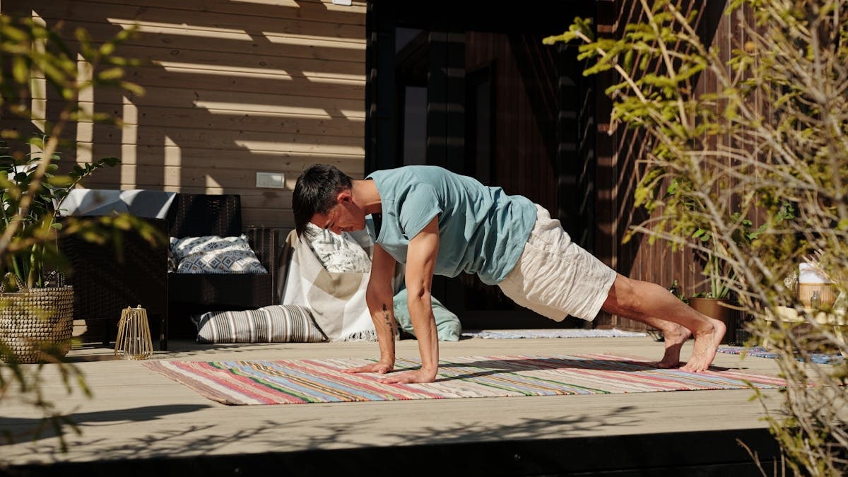 Adult man doing a plank exercise on a colorful yoga mat outdoors, promoting fitness and healthy living.